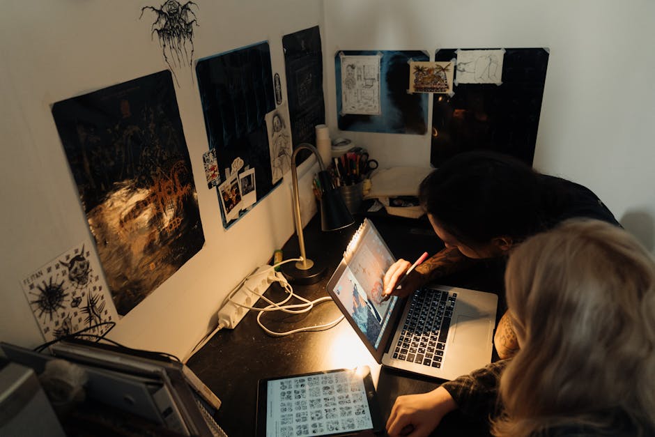 Two people collaborate on digital art at a cozy, well-lit home studio desk.
