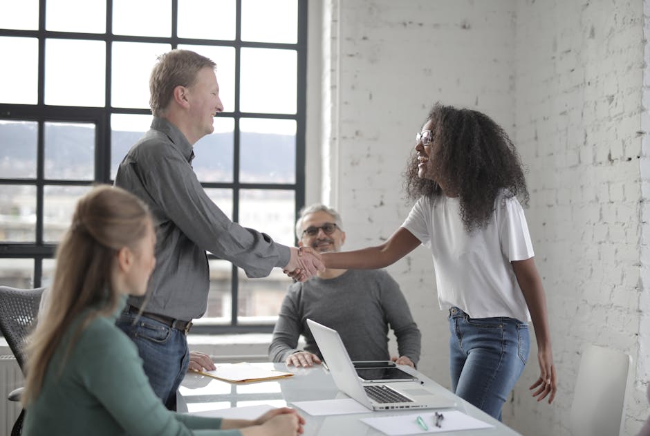 Young African American woman and mature man shaking hands while working in team and smiling with colleagues in modern workspace in daytime