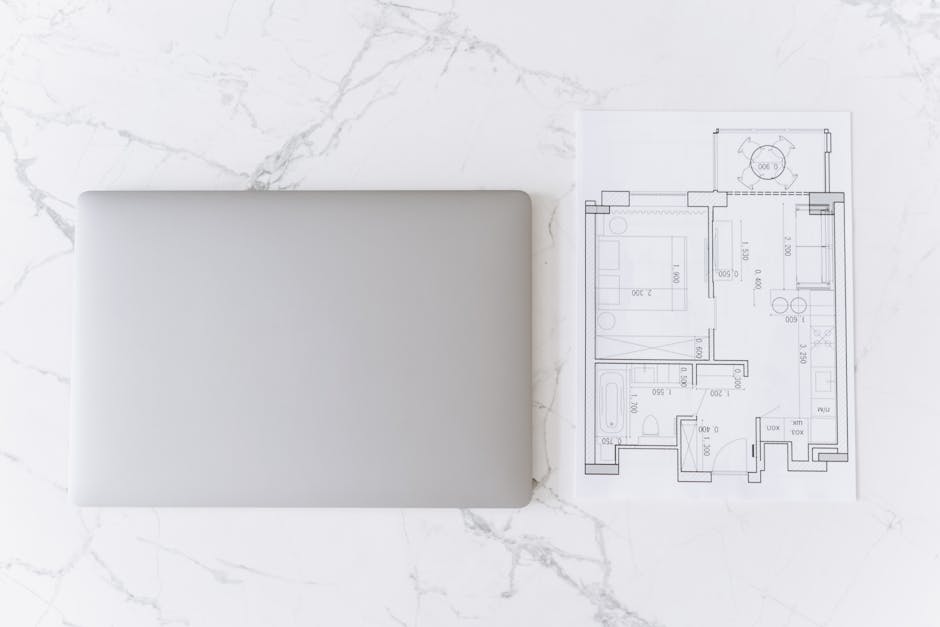 Top view of a laptop and architectural blueprint on white marble surface, showcasing modern workspace.