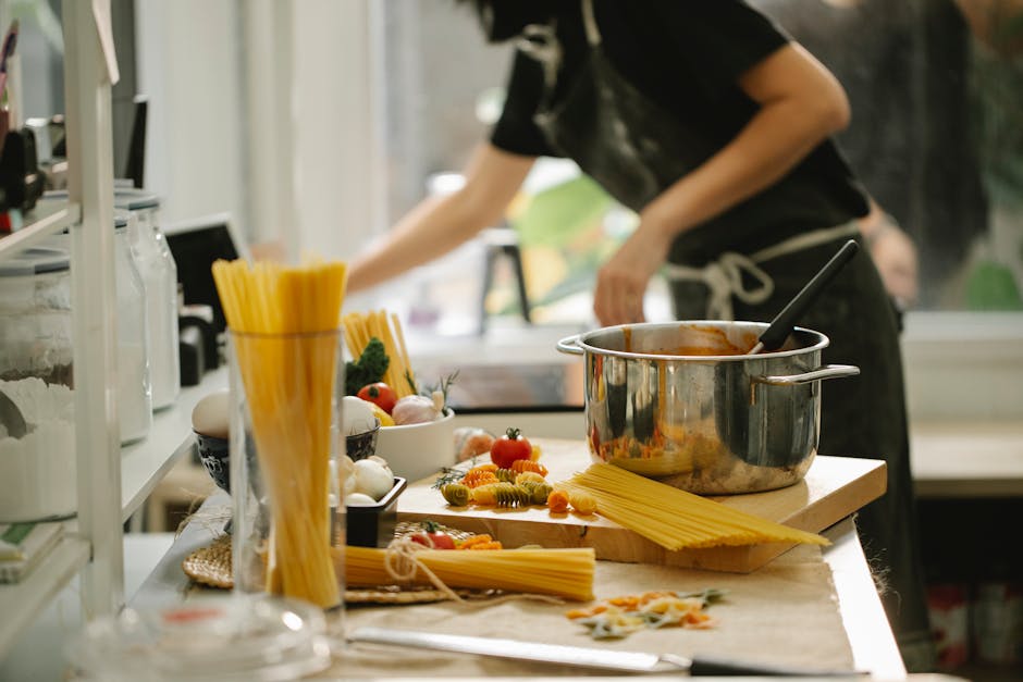 Side view crop anonymous female in apron cooking spaghetti in modern light kitchen