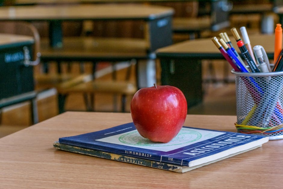 Red apple on books with stationery in a classroom, symbolizing education and knowledge.