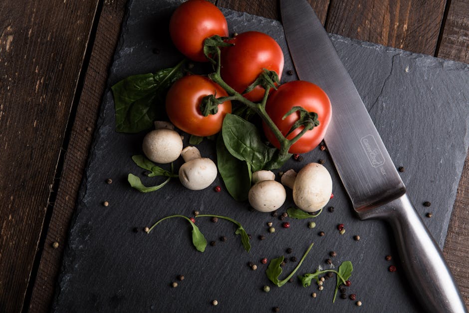 Top view of fresh tomatoes, mushrooms, and greens on a slate board with knife.