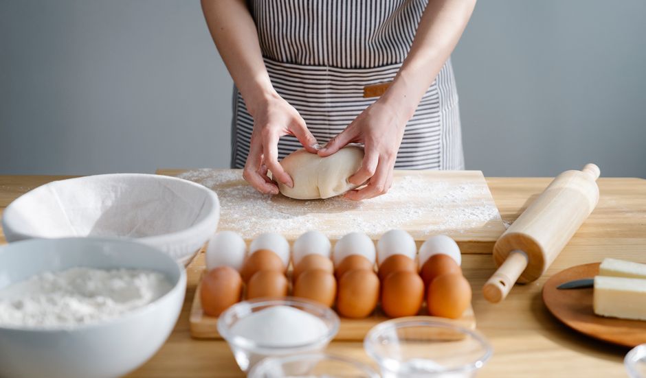 A woman in an apron kneading dough on a wooden table surrounded by baking ingredients