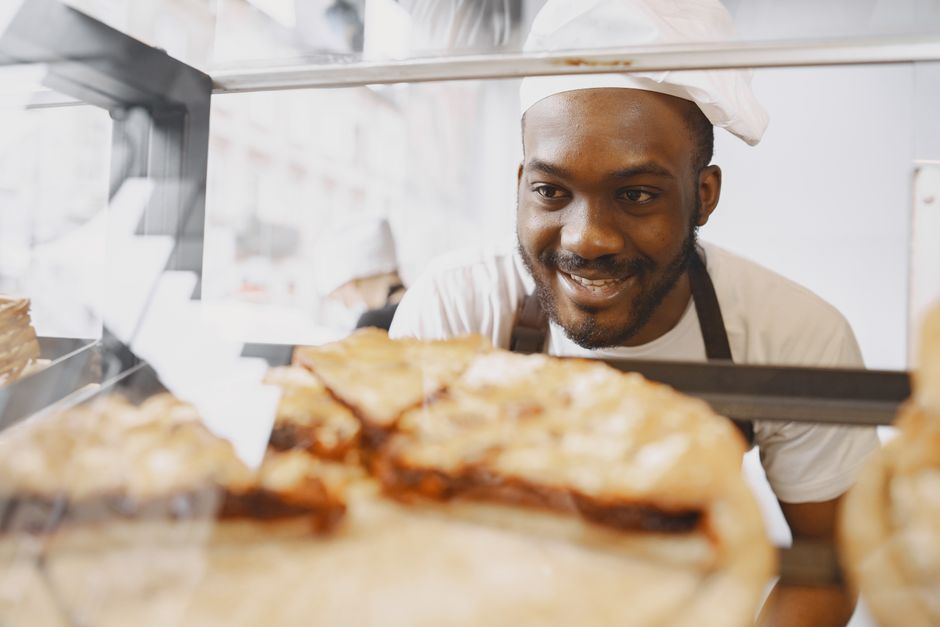 Baker smiling behind a glass counter filled with freshly baked pastries.