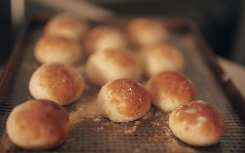 Close-up of freshly baked bread rolls on a baking tray, warm and golden brown.