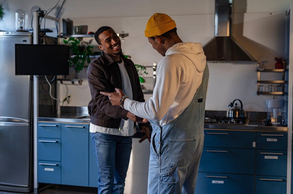 Two men exchanging friendly gestures in a contemporary kitchen space.