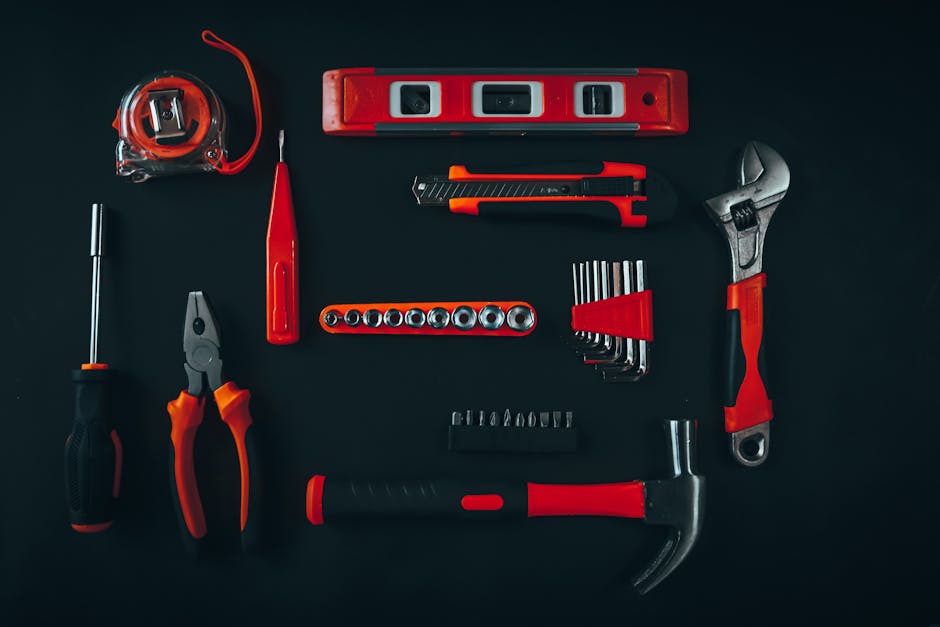 Top view arrangement of various repair tools including pliers hammer screwdriver and tape measure placed on black table