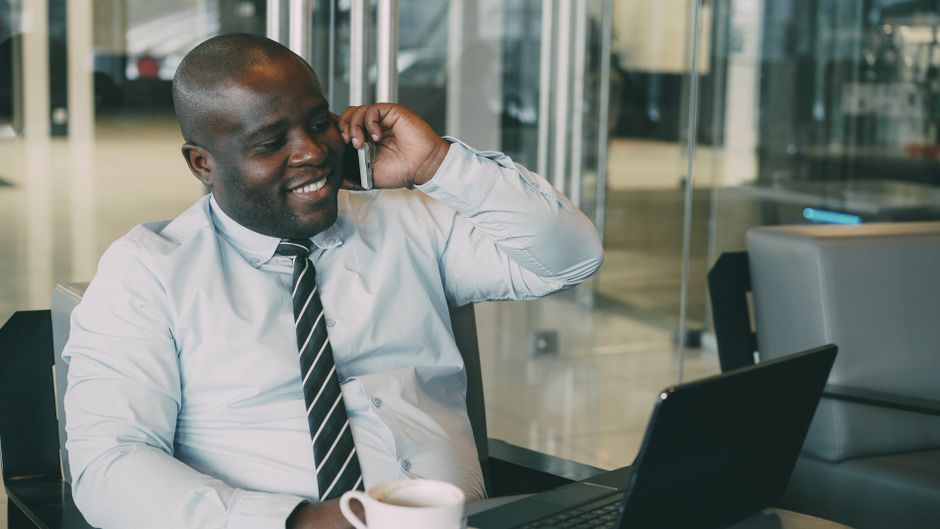Smiling businessman talking on the phone while working on laptop in modern office.
