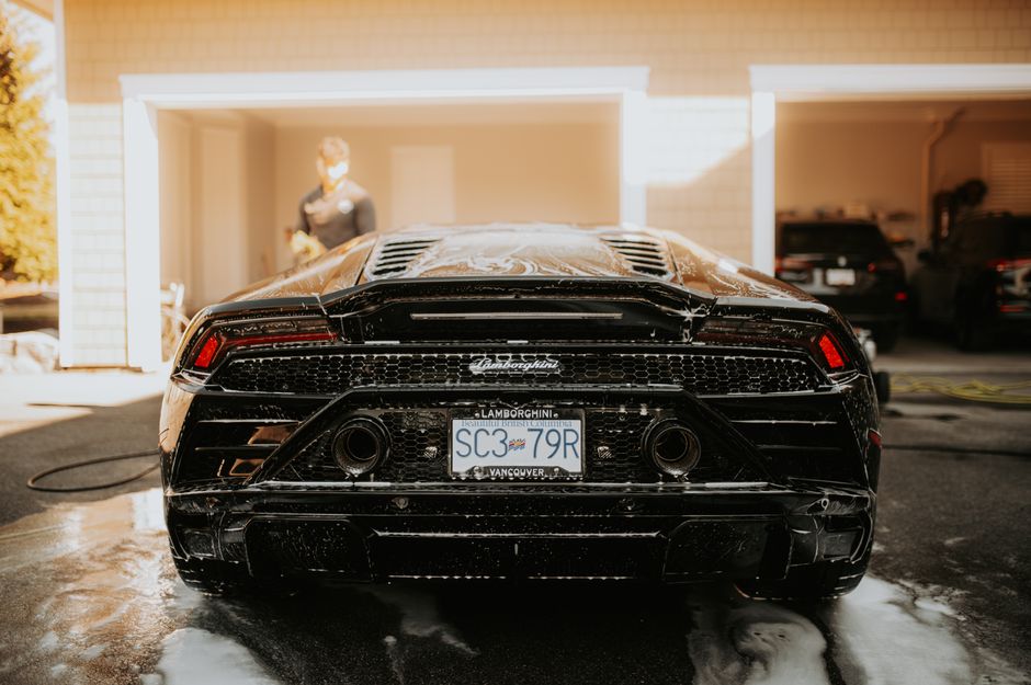 Rear view of a black Lamborghini being washed in a sunlit driveway in Vancouver.