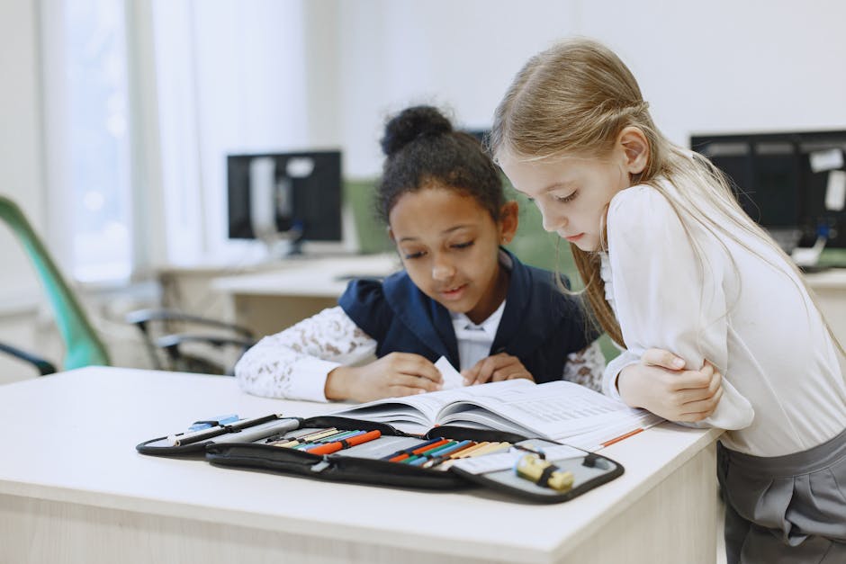 Two young girls studying together in a classroom, focused on reading and learning.