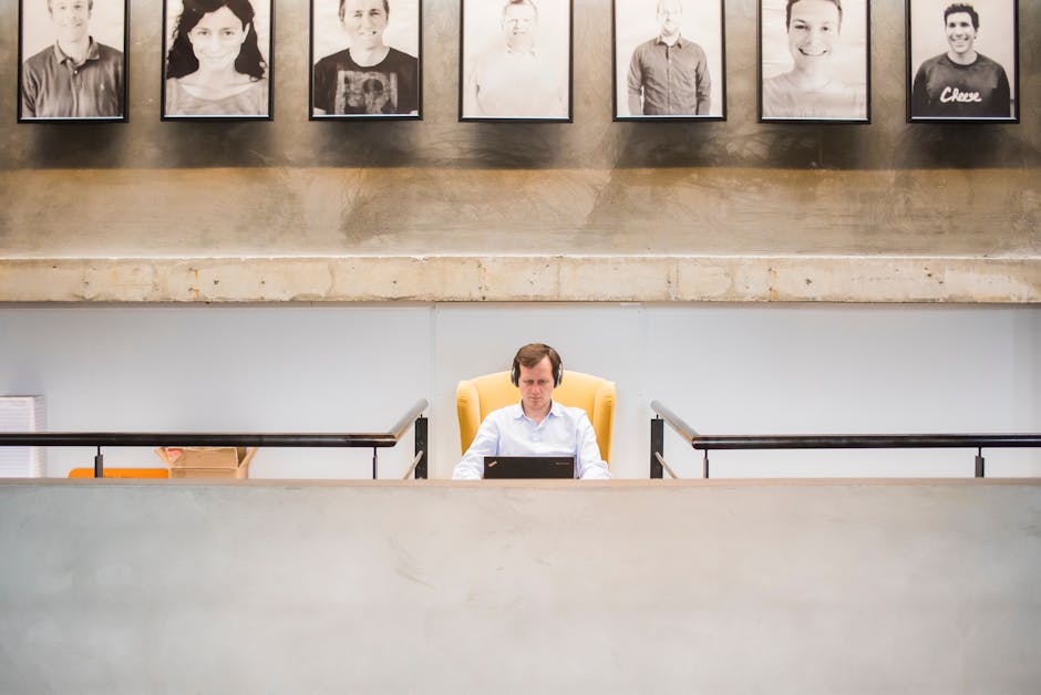 Business professional working on a laptop in a contemporary office setting with framed portraits above.