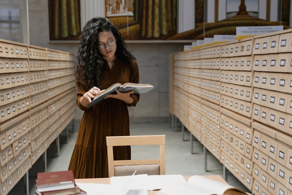A woman reading a book in a library archive room, surrounded by card catalogs.