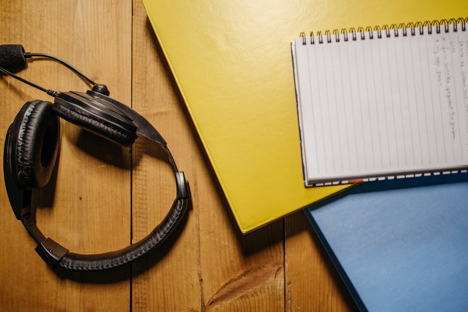 Flat lay of black headphones, a spiral notebook, and folders on a wooden surface.