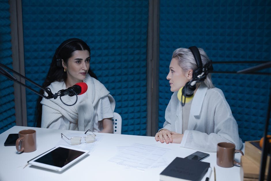 Two women engaged in a podcast recording session in a soundproof studio.