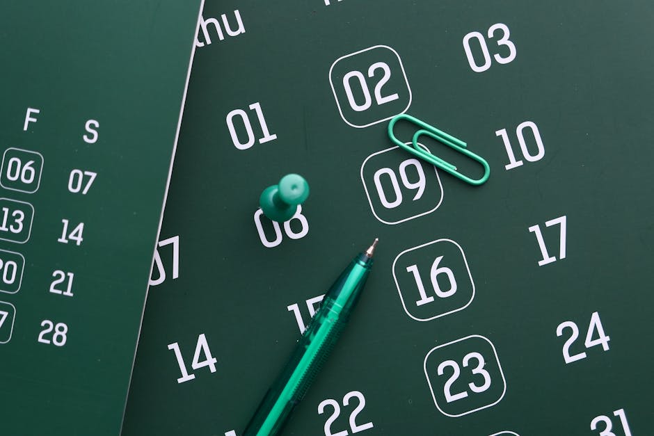 Close-up of a green calendar with pen, push pin, and paper clip for planning and organization.