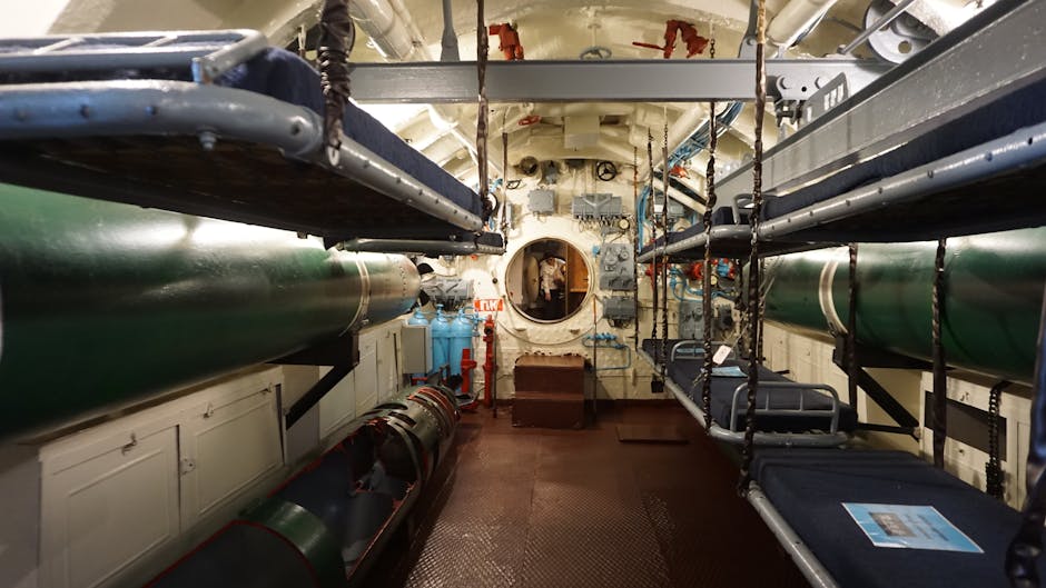 View of a submarine's bunk room with torpedo tubes and metal bunks.